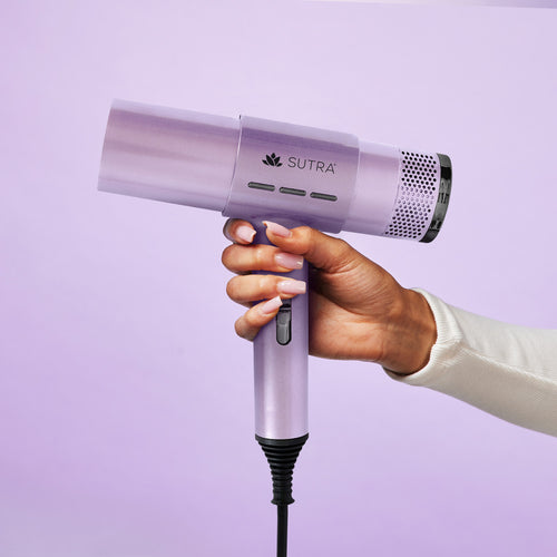 Hand-holding-lavender-airpro-blow-dryer-with-a-black-sutra-logo-on-a-light-purple-background