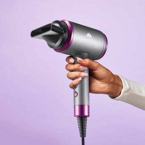 Hand-holding-silver-and-magenta-accelerator-3500-blow-dryer-with-nozzle-attached-on-a-purple-background