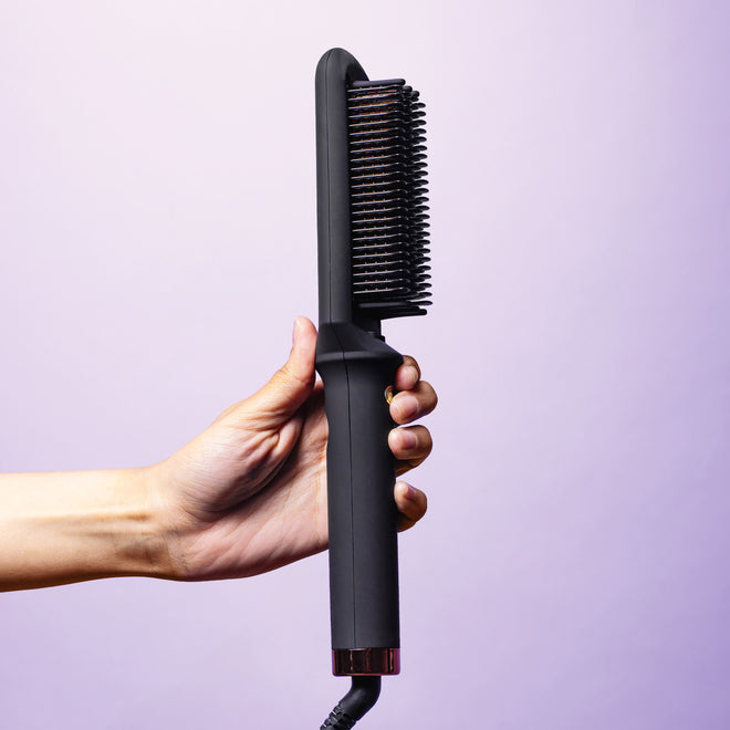 Hand-holding-black-Heated-Straightening-Brush-showing-the-side-profile-of-brush-on-purple-background